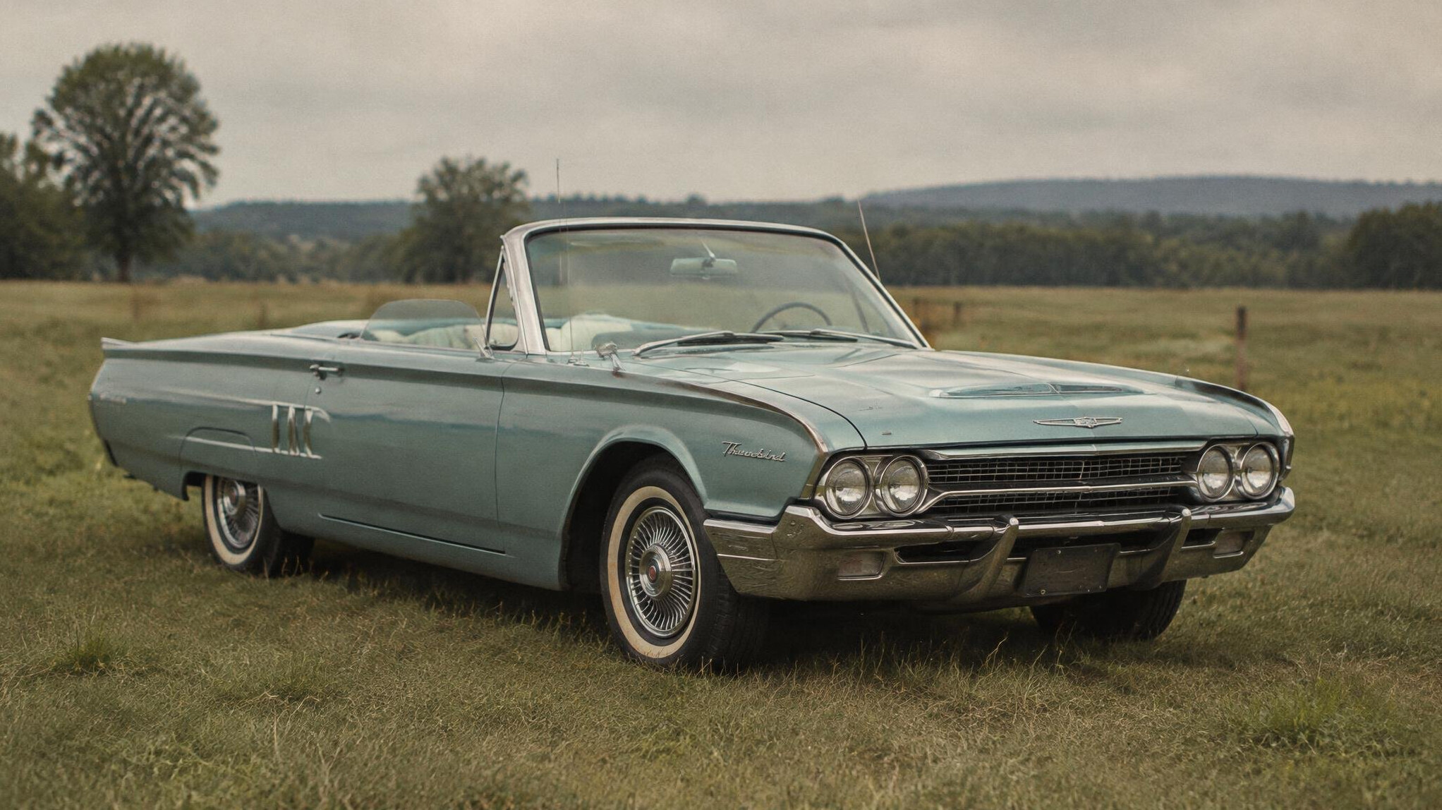 Archival style photograph of a 1960s classic convertible automobile parked in a field
